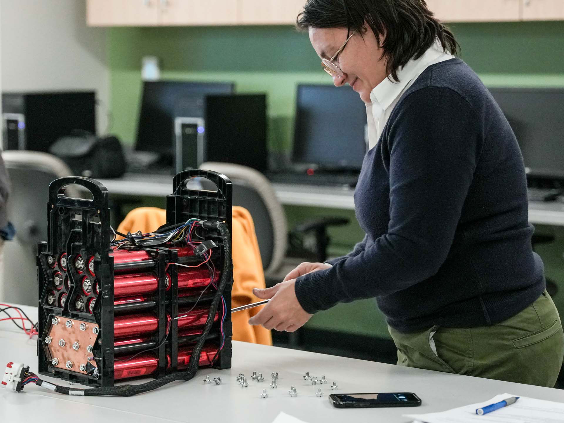 A woman in a computer lab assembles a small plastic tower containing several red batteries