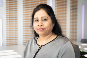 Female in business attire looks at camera, set in a modern lobby space.
